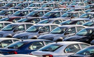 Rows of a new cars parked in a distribution center on a car factory on a sunny day. Parking in the open air. photo