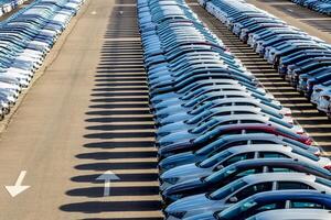 Rows of a new cars parked in a distribution center on a car factory on a sunny day. Top view to the parking in the open air. photo