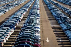 Rows of a new cars parked in a distribution center on a car factory on a sunny day. Top view to the parking in the open air. photo