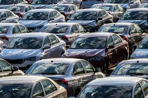 Rows of a new cars parked in a distribution center on a car factory on a sunny day. Top view to the parking in the open air. photo