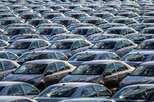 Rows of a new cars parked in a distribution center on a car factory on a sunny day. Top view to the parking in the open air. photo