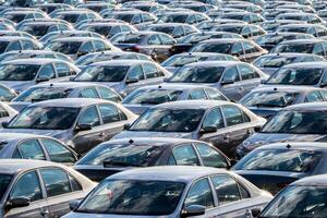 Rows of a new cars parked in a distribution center on a car factory on a sunny day. Top view to the parking in the open air. photo