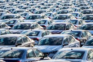 Rows of a new cars parked in a distribution center on a car factory on a sunny day. Top view to the parking in the open air. photo