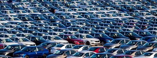Rows of a new cars parked in a distribution center on a car factory on a sunny day. Top view to the parking in the open air. photo