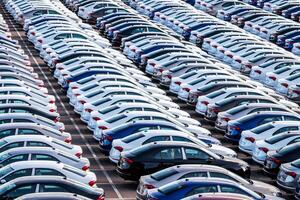 Rows of a new cars parked in a distribution center on a car factory on a sunny day. Top view to the parking in the open air. photo