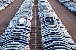 Rows of a new cars parked in a distribution center on a car factory on a sunny day. Top view to the parking in the open air. photo