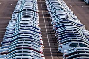 Rows of a new cars parked in a distribution center on a car factory on a sunny day. Top view to the parking in the open air. photo