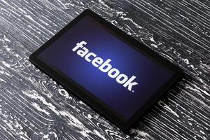 Tablet computer on a black wooden table with a social network facebook logo. photo