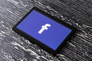Tablet computer on a black wooden table with a social network facebook logo. photo