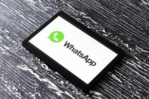 Tablet computer on a black wooden table with a messenger WhatsApp logo on the screen. photo