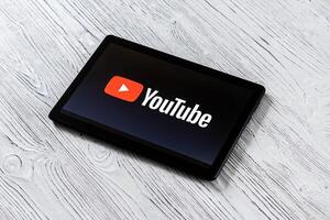 Black tablet computer on a white wooden table with a social network YouTube logo on the screen. photo