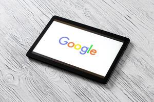 Black tablet computer on a white wooden table with a search system google logo on the screen. photo