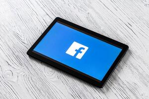 Black tablet computer on a white wooden table with a social network facebook logo on the screen. photo