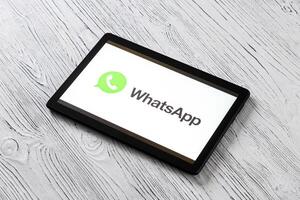 Black tablet computer on a white wooden table with a messenger WhatsApp logo on the screen. photo