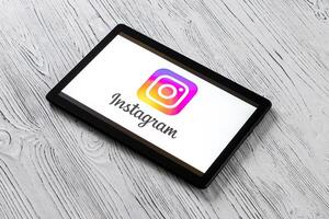 Black tablet computer on a white wooden table with a social network instagram logo on the screen. photo