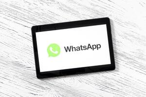 Black tablet computer on a white wooden table with a messenger WhatsApp logo on the screen. photo