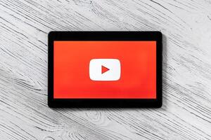 Black tablet computer on a white wooden table with a social network YouTube logo on the screen. photo
