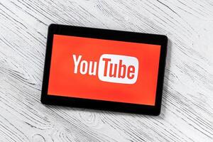 Black tablet computer on a white wooden table with a social network YouTube logo on the screen. photo