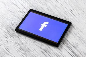 Black tablet computer on a white wooden table with a social network facebook logo on the screen. photo