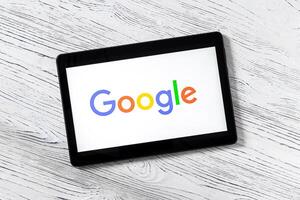 Black tablet computer on a white wooden table with a search system google logo on the screen. photo