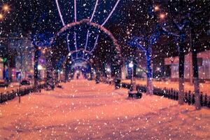 Blured photo of a winter night park with lanterns and Christmas decorations in snowfall.