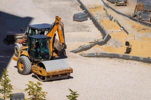 Russia, Kaluga - OCTOBER 27, 2020 Tractor with a bucket and asphalt roller leveling gravel for construction. photo