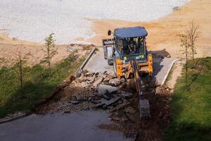 Russia, Kaluga - OCTOBER 27, 2020 Tractor breaking the old asphalt with a bucket before the construction. photo