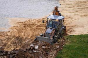 Russia, Kaluga - OCTOBER 27, 2020 Tractor breaking the old asphalt with a bucket before the construction. photo