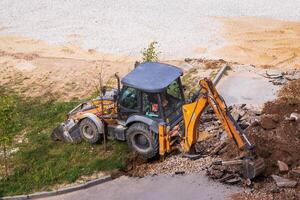 Russia, Kaluga - OCTOBER 27, 2020 Tractor breaking the old asphalt with a bucket before the construction. photo