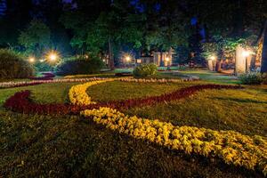 A night park lit by lanterns with a stone pavement, trees, fallen leaves and benches in early autumn. photo