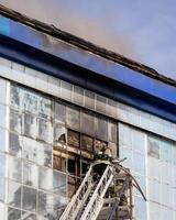 Russia, Kaluga - SEPTEMBER 08, 2020 A team of firefighters in protective suits and helmets on the stairs extinguishing a fire in a building with a broken window. photo