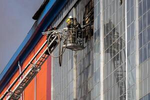 Russia, Kaluga - SEPTEMBER 08, 2020 A team of firefighters in protective suits and helmets on the stairs extinguishing a fire in a building with a broken window. photo