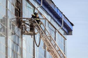 Russia, Kaluga - SEPTEMBER 08, 2020 A team of firefighters in protective suits and helmets on the stairs extinguishing a fire in a building with a broken window. photo
