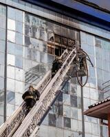 Russia, Kaluga - SEPTEMBER 08, 2020 A team of firefighters in protective suits and helmets on the stairs extinguishing a fire in a building with a broken window. photo