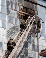 Russia, Kaluga - SEPTEMBER 08, 2020 A team of firefighters in protective suits and helmets on the stairs extinguishing a fire in a building with a broken window. photo
