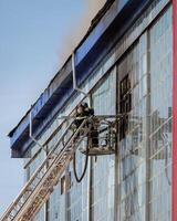 Russia, Kaluga - SEPTEMBER 08, 2020 A team of firefighters in protective suits and helmets on the stairs extinguishing a fire in a building with a broken window. photo