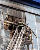 Russia, Kaluga - SEPTEMBER 08, 2020 A team of firefighters in protective suits and helmets on the stairs extinguishing a fire in a building with a broken window. photo