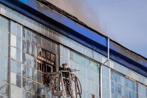 Russia, Kaluga - SEPTEMBER 08, 2020 A team of firefighters in protective suits and helmets on the stairs extinguishing a fire in a building with a broken window. photo