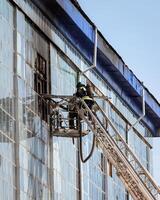 Russia, Kaluga - SEPTEMBER 08, 2020 A team of firefighters in protective suits and helmets on the stairs extinguishing a fire in a building with a broken window. photo
