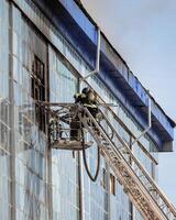 Russia, Kaluga - SEPTEMBER 08, 2020 A team of firefighters in protective suits and helmets on the stairs extinguishing a fire in a building with a broken window. photo