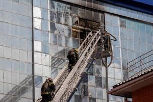 Russia, Kaluga - SEPTEMBER 08, 2020 A team of firefighters in protective suits and helmets on the stairs extinguishing a fire in a building with a broken window. photo