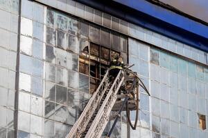 Russia, Kaluga - SEPTEMBER 08, 2020 A team of firefighters in protective suits and helmets on the stairs extinguishing a fire in a building with a broken window. photo