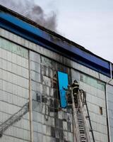 Russia, Kaluga - SEPTEMBER 08, 2020 A team of firefighters in protective suits and helmets on the stairs extinguishing a fire in a building with a broken window. photo
