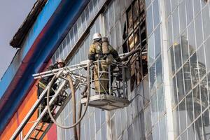 Russia, Kaluga - SEPTEMBER 08, 2020 A team of firefighters in protective suits and helmets on the stairs extinguishing a fire in a building with a broken window. photo