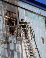 Russia, Kaluga - SEPTEMBER 08, 2020 A team of firefighters in protective suits and helmets on the stairs extinguishing a fire in a building with a broken window. photo