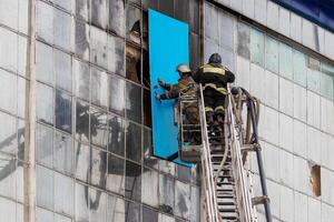 Russia, Kaluga - SEPTEMBER 08, 2020 A team of firefighters in protective suits and helmets on the stairs extinguishing a fire in a building with a broken window. photo