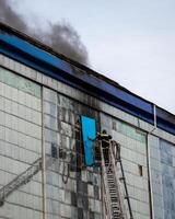 Russia, Kaluga - SEPTEMBER 08, 2020 A team of firefighters in protective suits and helmets on the stairs extinguishing a fire in a building with a broken window. photo