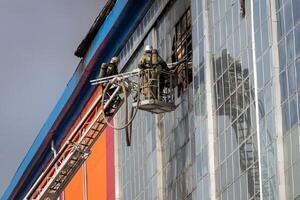 Russia, Kaluga - SEPTEMBER 08, 2020 A team of firefighters in protective suits and helmets on the stairs extinguishing a fire in a building with a broken window. photo