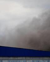 Black smoke rising from a burning building with a cloudy sky. photo