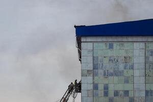 Russia, Kaluga - SEPTEMBER 08, 2020 A team of firefighters in protective suits and helmets on the stairs extinguishing a fire in a building with a broken window. photo
